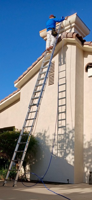 A Kern Painting crew member on a tall ladder painting the roofline of a stucco home