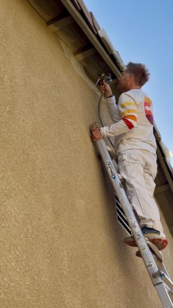 Nate on a ladder spraying the eaves of a stucco house