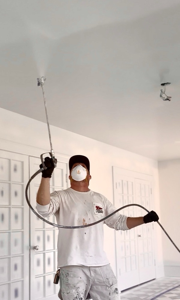 A Kern Painting crew member spraying a ceiling in a freshly painted white room
