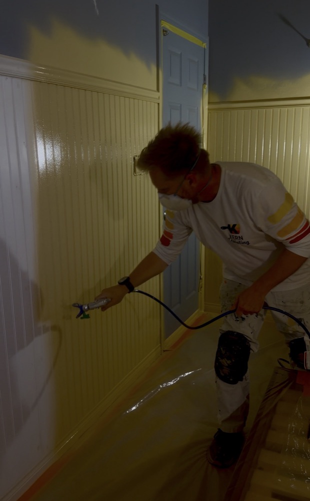 Nate spraying finish coat on beadboard wainscoting in a hallway