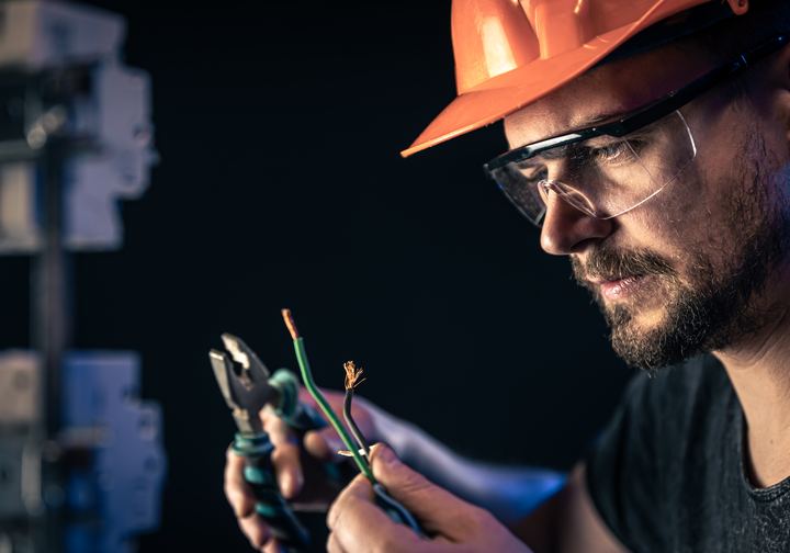 Electrician in an orange hard hat holding wire and pliers