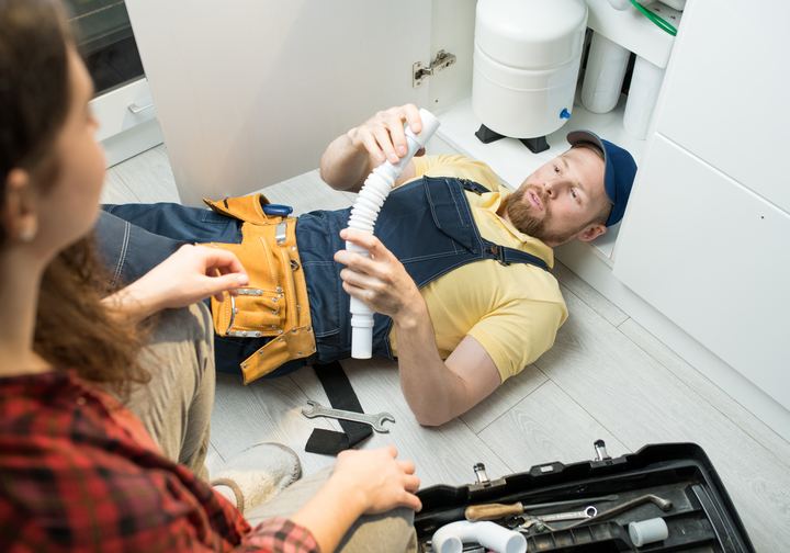 Plumber on the floor fitting a drain pipe under a sink